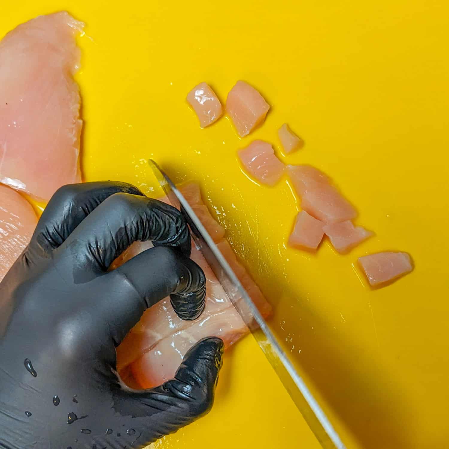 chicken breast slices being cut into small dices.